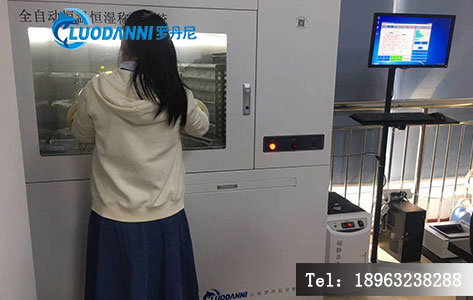 实验室工作台上凌乱摆放着多张待称重的滤膜,与学生正在调整老款手动天平形成对比,凸显自动化需求